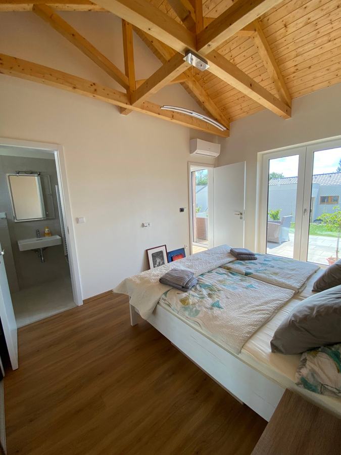 Postel pod dřevěným krovem a okno do zahrady
